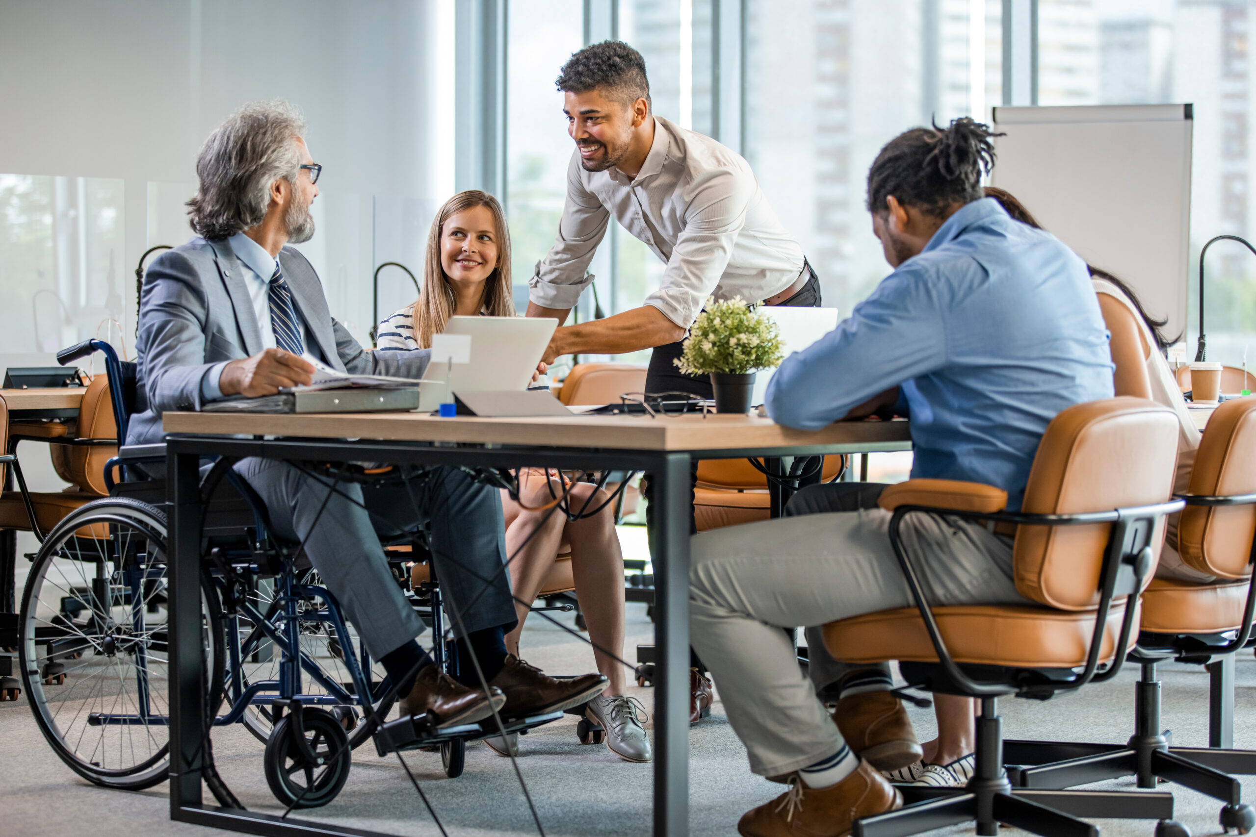 selective focus of smiling disabled businessman and colleagues in office. side view of a disabled businessman. young businessman greeting handicapped business partner and team. coworker on wheelchair