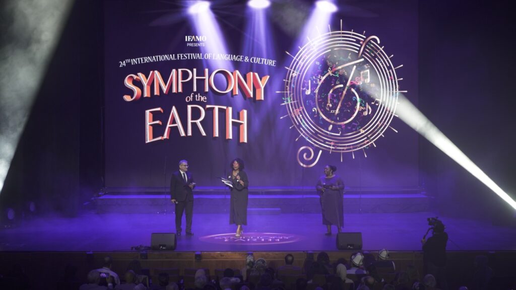 Hosts on stage in front of the Symphony of the Earth title screen at the 24th International Festival of Language and Culture